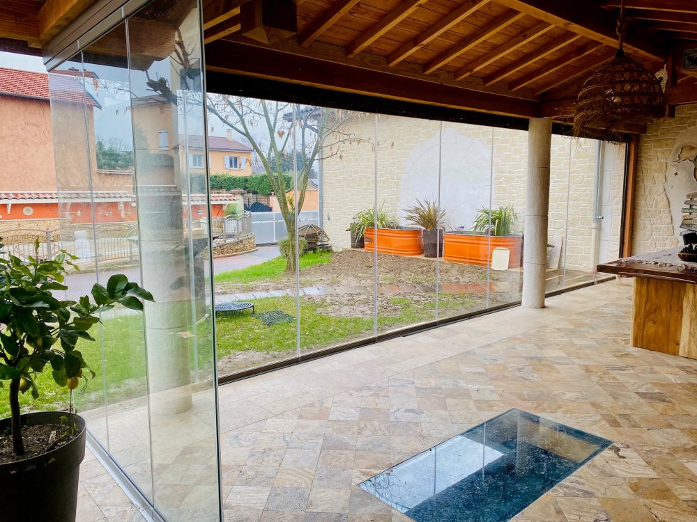 Conception et installation d’un système de fermeture de terrasse sur-mesure, harmonieusement intégré à cette habitation située dans l’Ain (01).