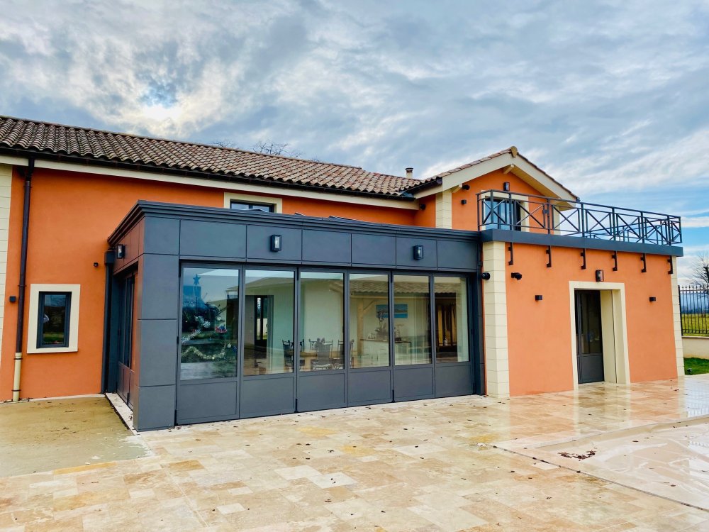 Rénovation et extension d’une habitation d’exception près de Villefranche-sur-Saône (69), intégrant des baies accordéon, une toiture vitrée et des stores sur-mesure.